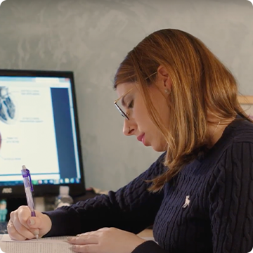 Image shows young lady sat at a computer and revising