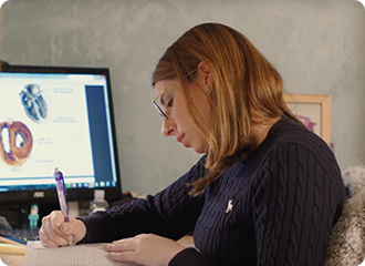 Image shows young lady sat at a computer and revising